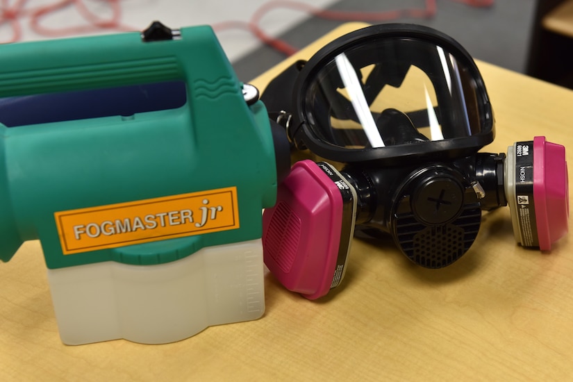 A mask and a hand-held machine with the words "Fogmaster Jr." rest on a table.