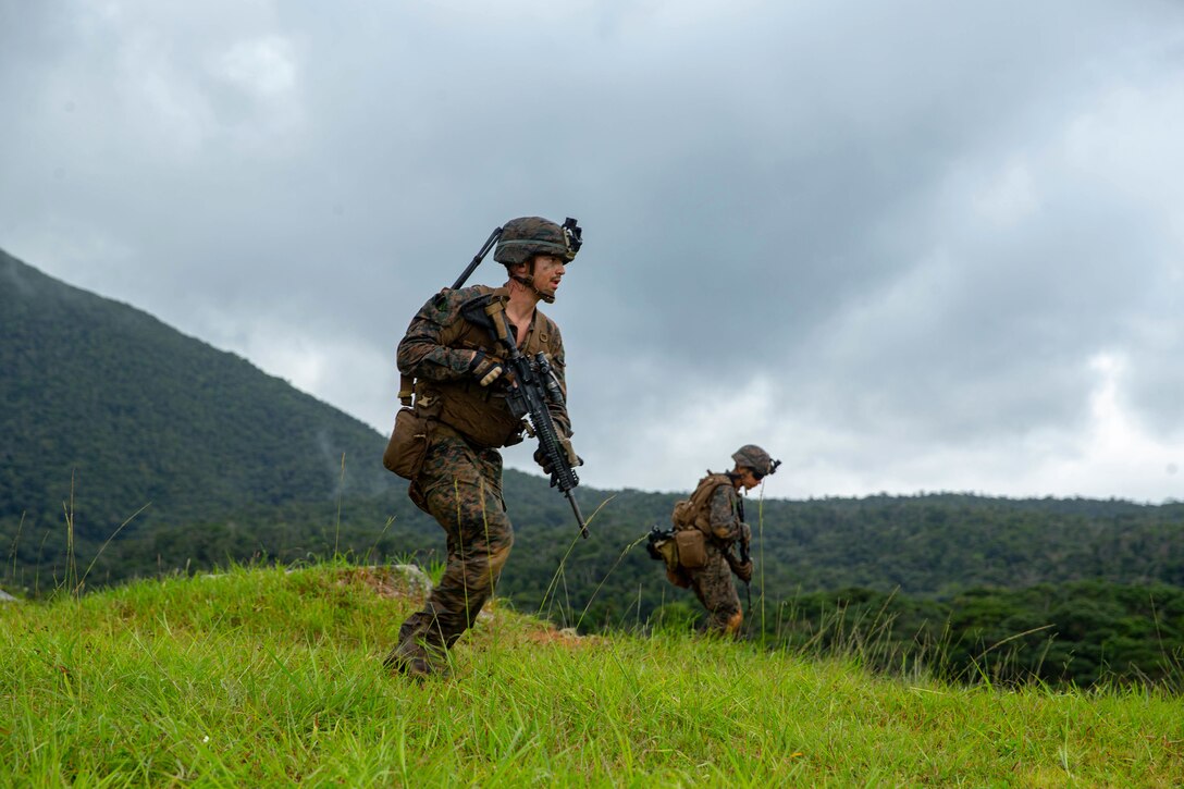 Two Marines hold weapons while standing in a field-like area.