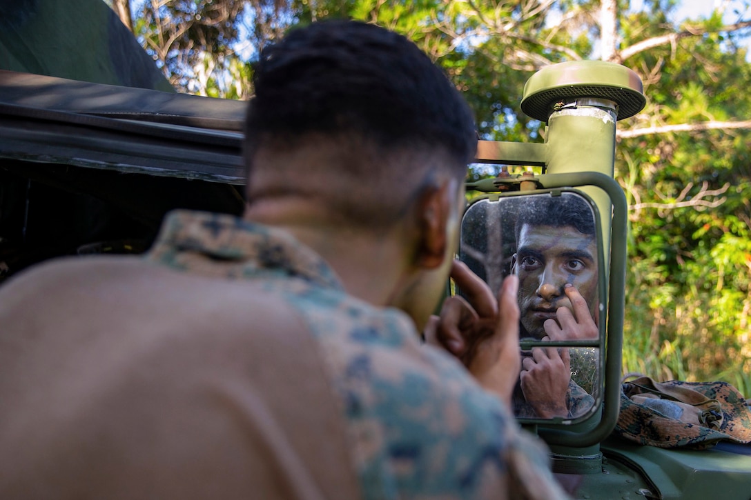 A Marine puts on camouflage paint on his face while looking in the mirror.