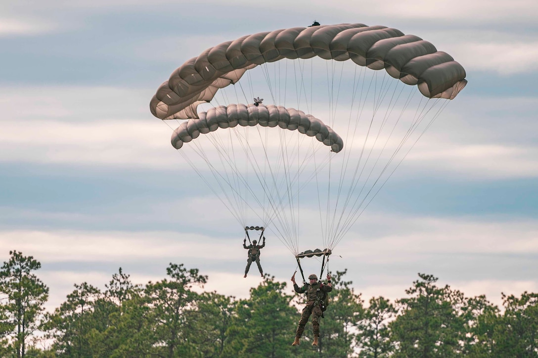 Two Marines descend in the sky wearing parachutes.