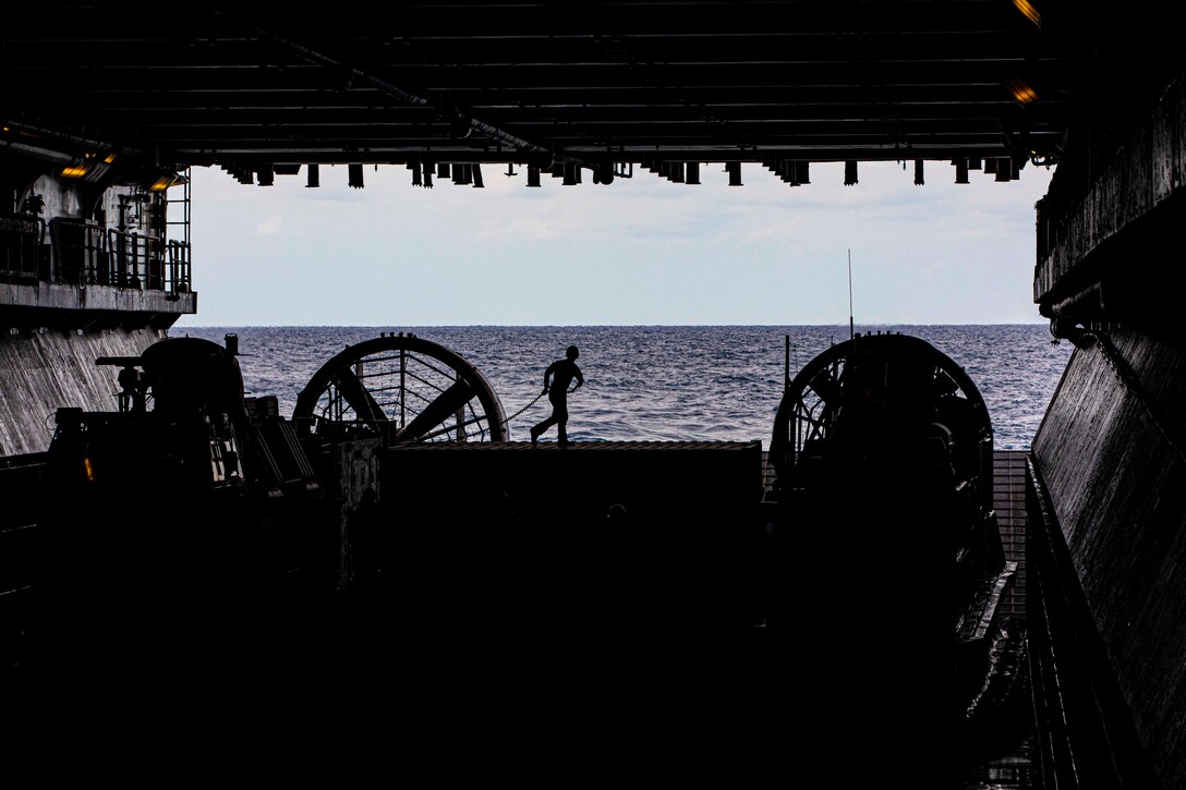 A sailor, shown in silhouette, runs aboard a ship; the ocean seen in the background.