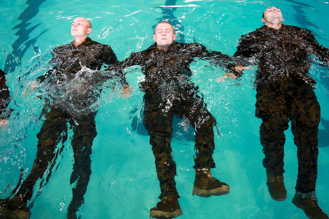 Three Marines float on their backs in a pool.