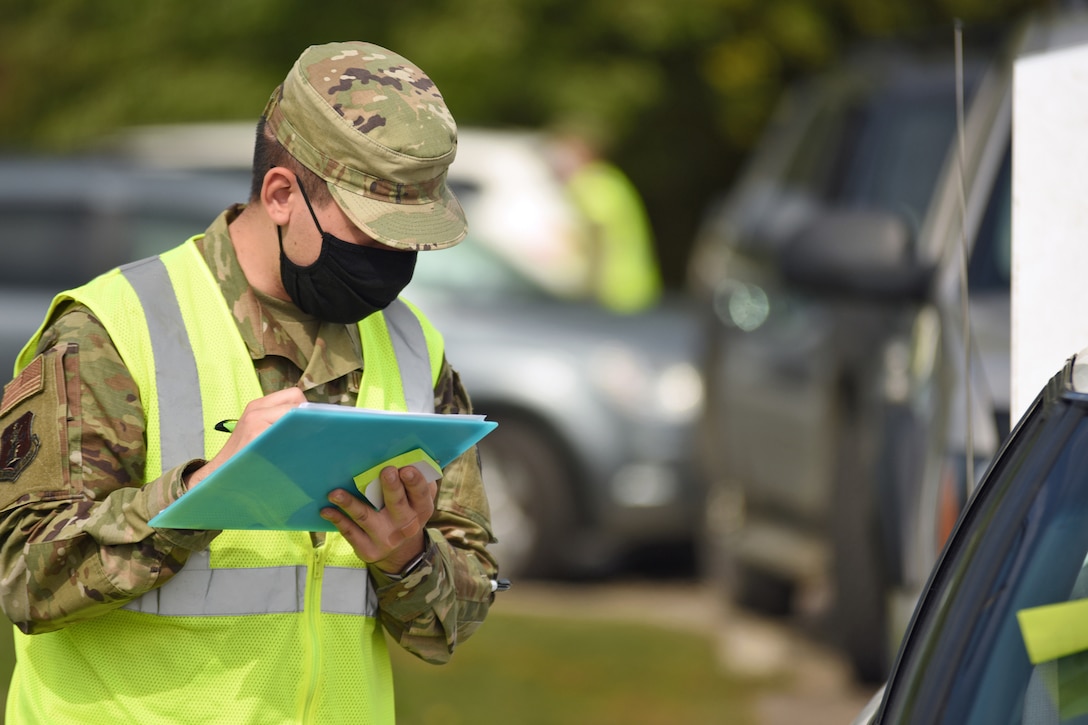 A male guardsman wearing a face mask takes inventory of prepared boxes of groceries loaded into vehicles.