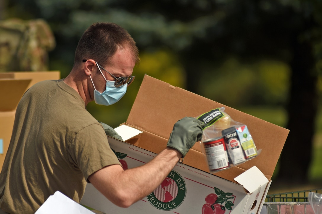 A male guardsman wearing a face mask and gloves prepares boxes of groceries.