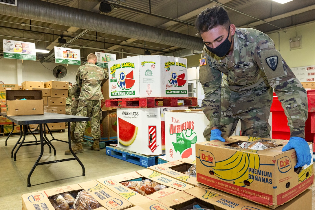 A male guardsman wearing a face mask and gloves moves a box of food.