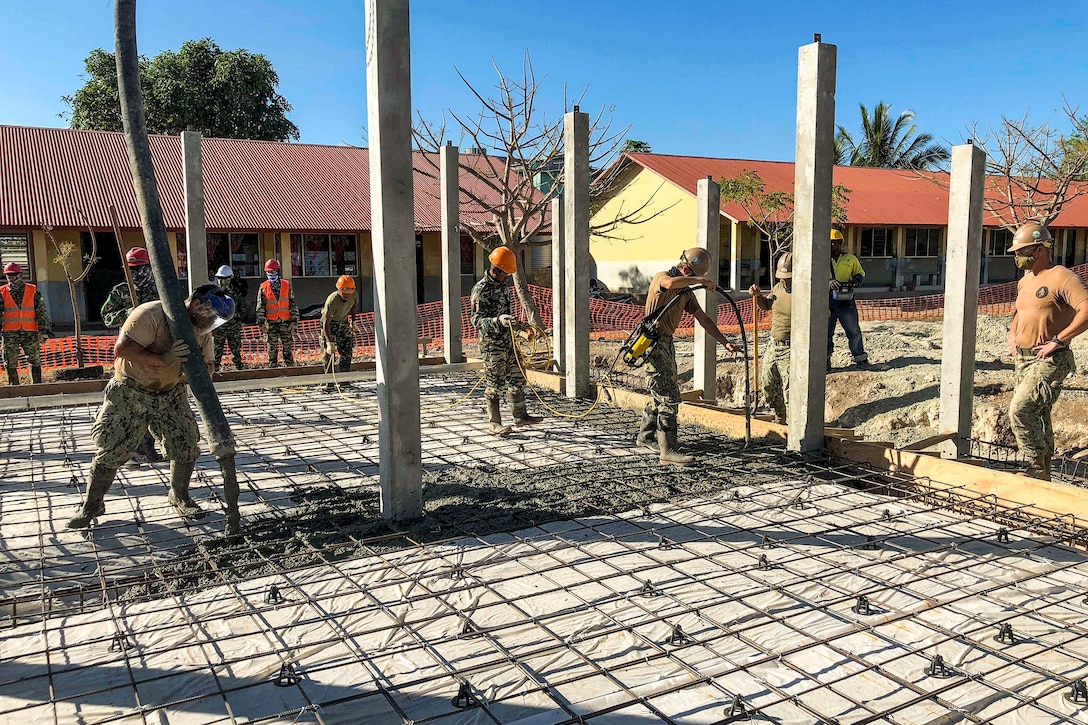 Service members wearing hardhats work at a construction site.