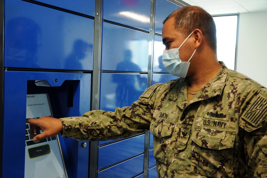 A male seaman wearing a face mask keys in a code on a mail locker.