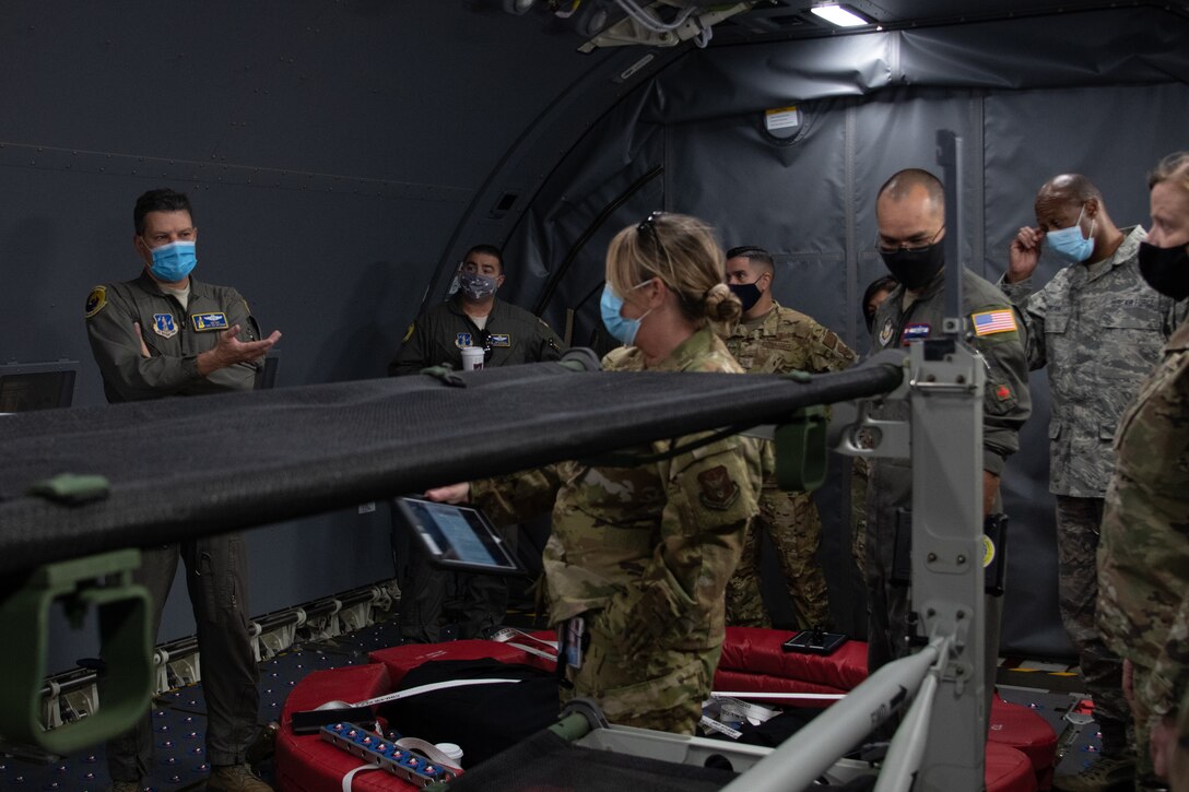 An Airman in a flight uniform speaks to a small audience inside of a cargo aircraft with a medical litter modification on display.
