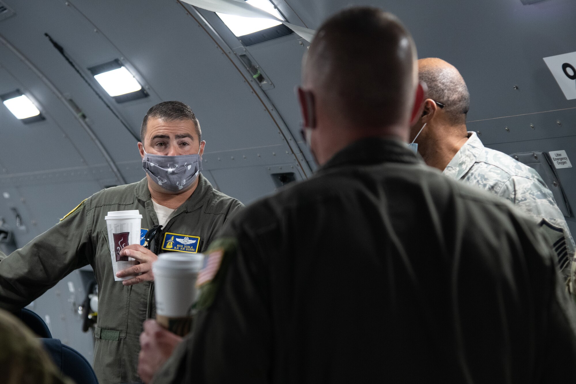 An Airman in a flight uniform speaks to two men inside of a cargo aircraft.