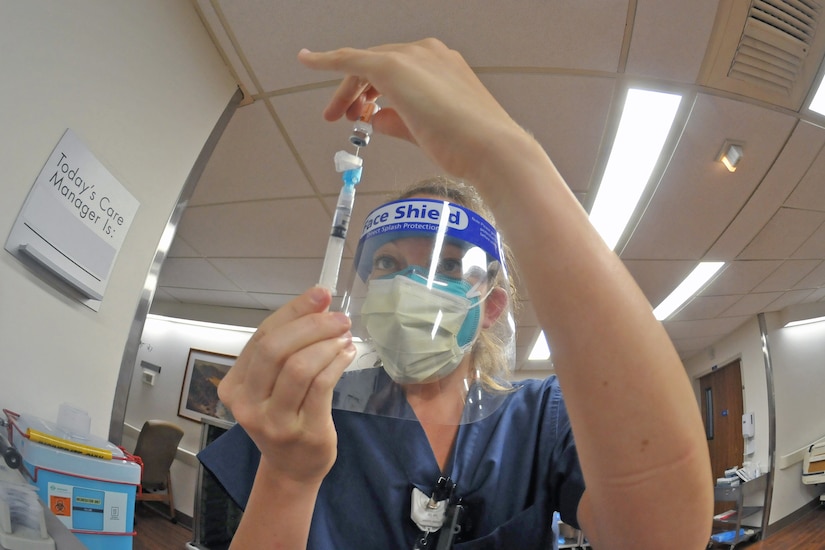 A woman wearing personal protective equipment fills a syringe.