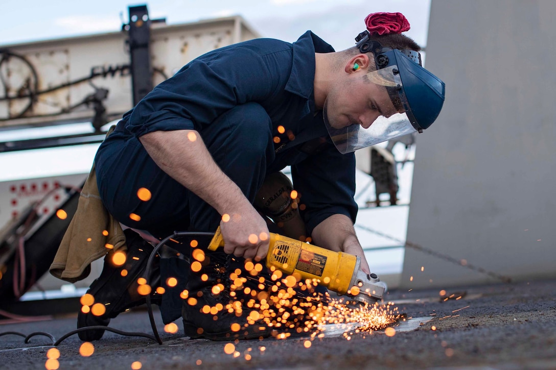 Sparks fly as a sailor uses a piece of equipment to grind the deck of a ship.