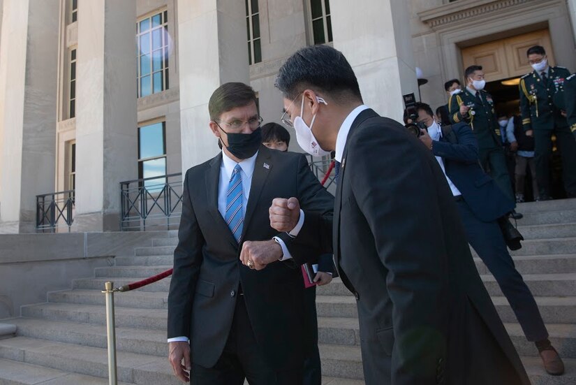 Men, wearing face masks, touch elbows in greeting.