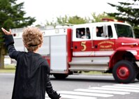 A child waves at members of the 35th Civil Engineer Squadron Fire Department during a parade concluding Fire Prevention Week, at Misawa Air Base, Japan, Oct. 8, 2020. Fire Prevention Week gave firefighters an opportunity to connect with the community without being on emergency call. (U.S. Air Force photo by Staff Sgt. Grace Nichols)