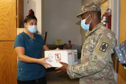 Jessica Robinson, Doniphan County Health Department and Home Health office manager, transfers a box of COVID-19 test samples to Spc. Adrian Turner, Kansas Army National Guard automated logistical specialist, 997th Brigade Support Battalion, in Troy, Kansas, July 27, 2020. Kansas National Guard teams have been transporting COVID-19 samples from across the state to the KDHE lab since March.