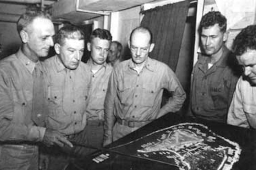 A Marine officer briefs others using a large, table-top map.