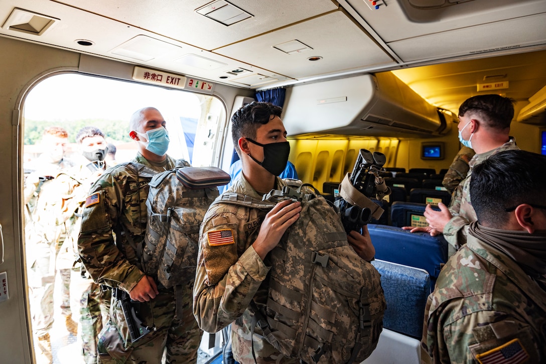 Soldiers wearing face masks board an airplane.