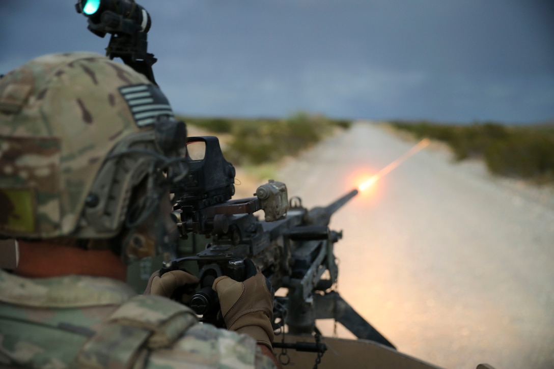 A soldier fires a weapon in a desert-like area.