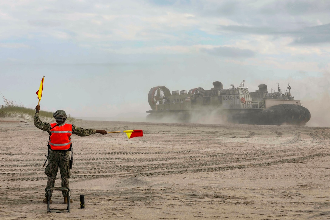 A sailor signals a vehicle on a beach.