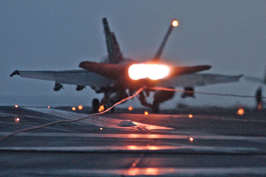 An aircraft lands on the deck of a large navy ship.