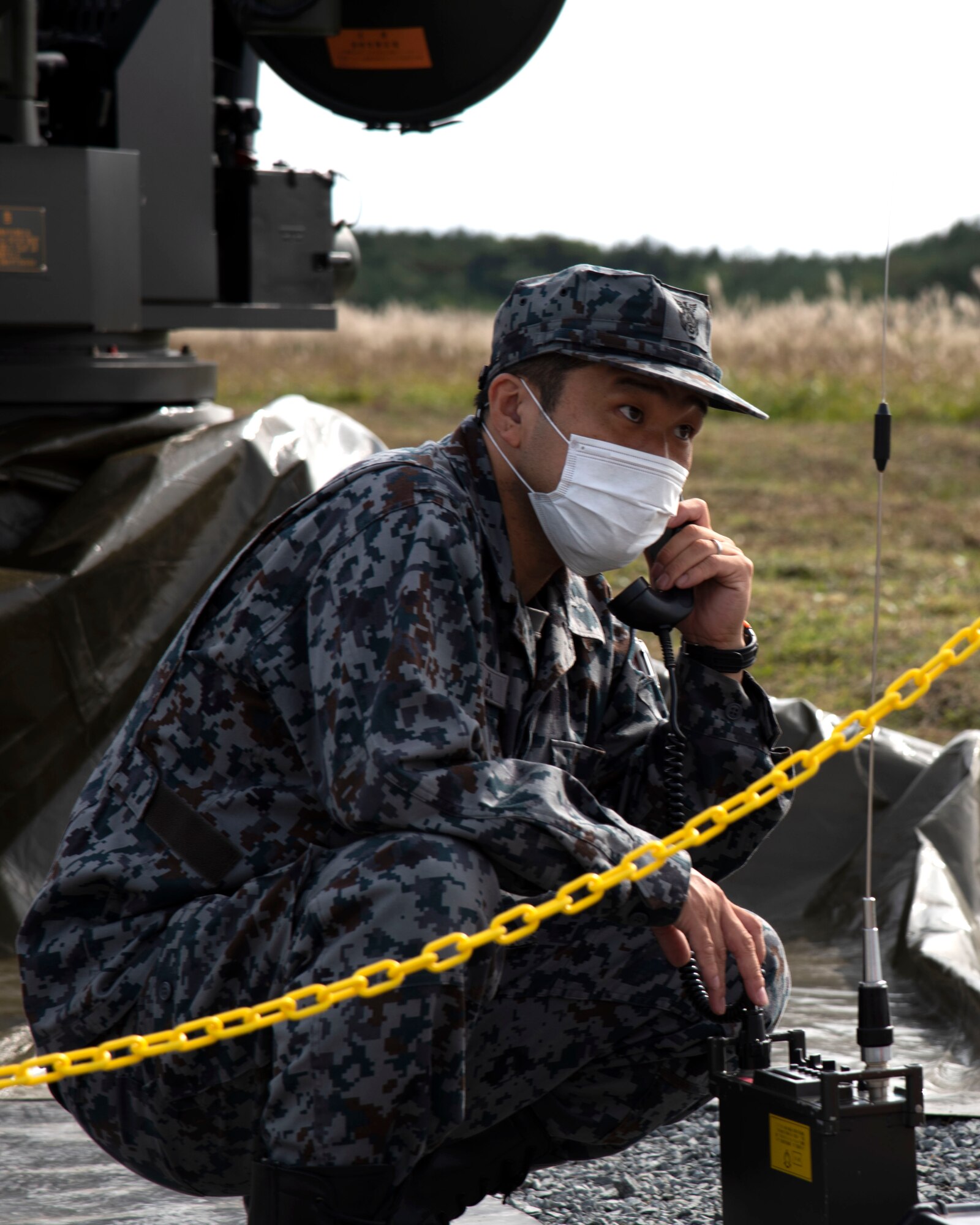 A man in uniform kneels outside while talking on a corded phone