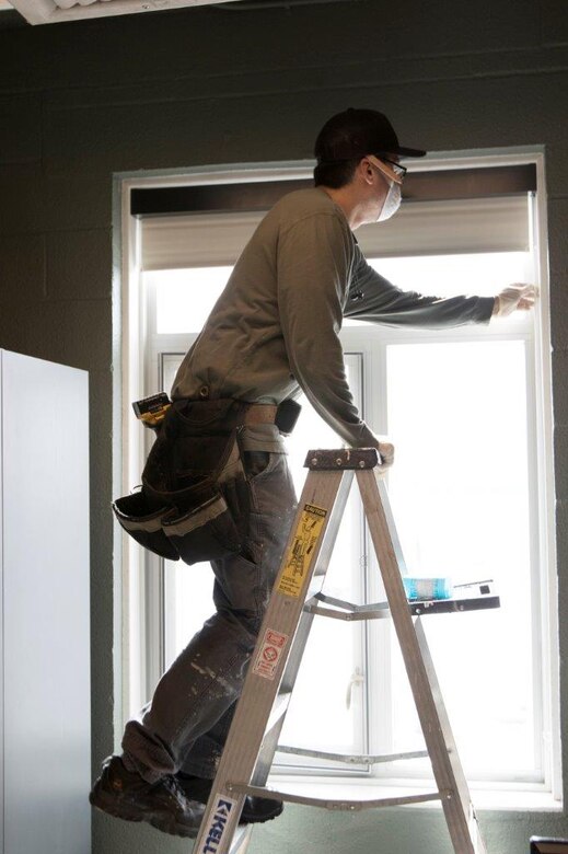 A worker installs a blackout shade in a barrack on Fort Wainwright in March 2020.