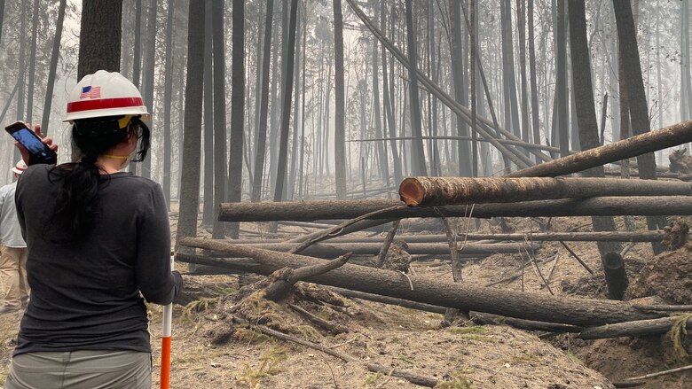 Erica Medley, a dam safety geologist with Portland District, U.S. Army Corps of Engineers, makes her way through thick smoke and fallen trees as she surveys damage on site at Blue River Dam Sept. 14. Medley joined a multi-disciplinary team of operations, engineering and dam safety personnel for a detailed inspection of the project just days after the Holiday Farm Fire burned through the area, impacting Blue River and nearby Cougar Dam.