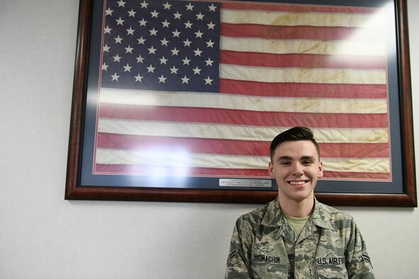 An Airman poses for a photo in front of a flag.