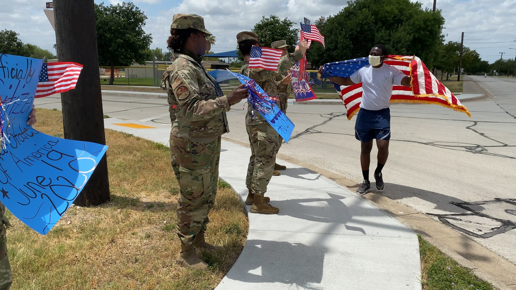 Members of the 47th Operations Support Squadron hold up signs and congratulate Airman 1st Class Gaddiel Acquaah, a 47th Operations Support Squadron aerospace physiology technician, on obtaining his U.S. citizenship at Laughlin Air Force Base, Texas, June 26, 2020. Acquaah’s leadership and flight planned the drive-by celebration to mitigate the spread of COVID-19. (U.S. Air Force photo by Senior Airman Marco A. Gomez)