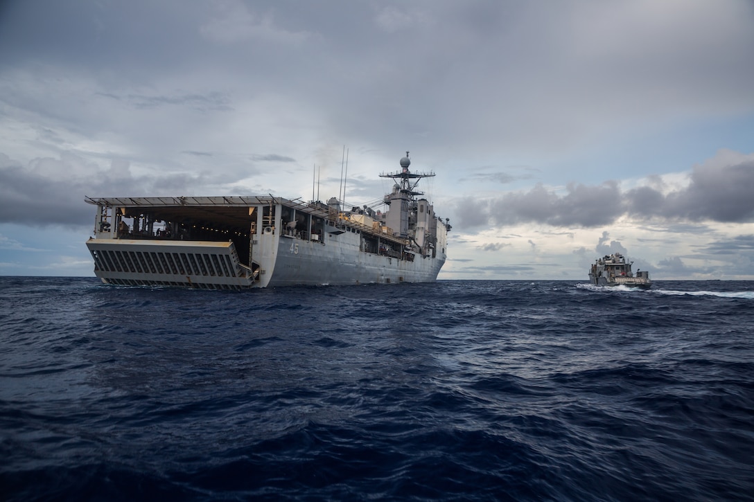 A small patrol boat steams next to a larger military ship in the ocean.