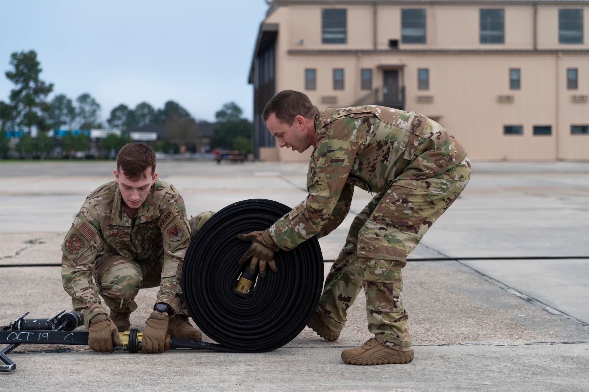 A photo of two airmen rolling up a fuel hose.