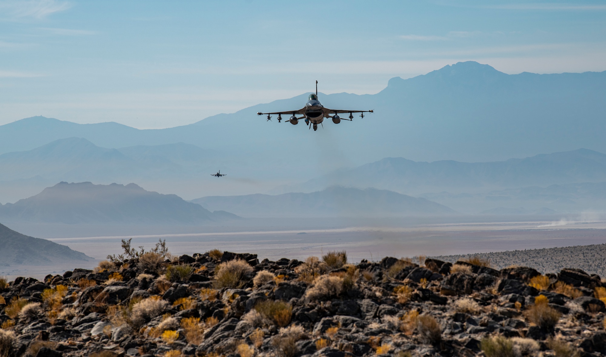 F-16 Fighting Falcon fighter jets fly over hill.