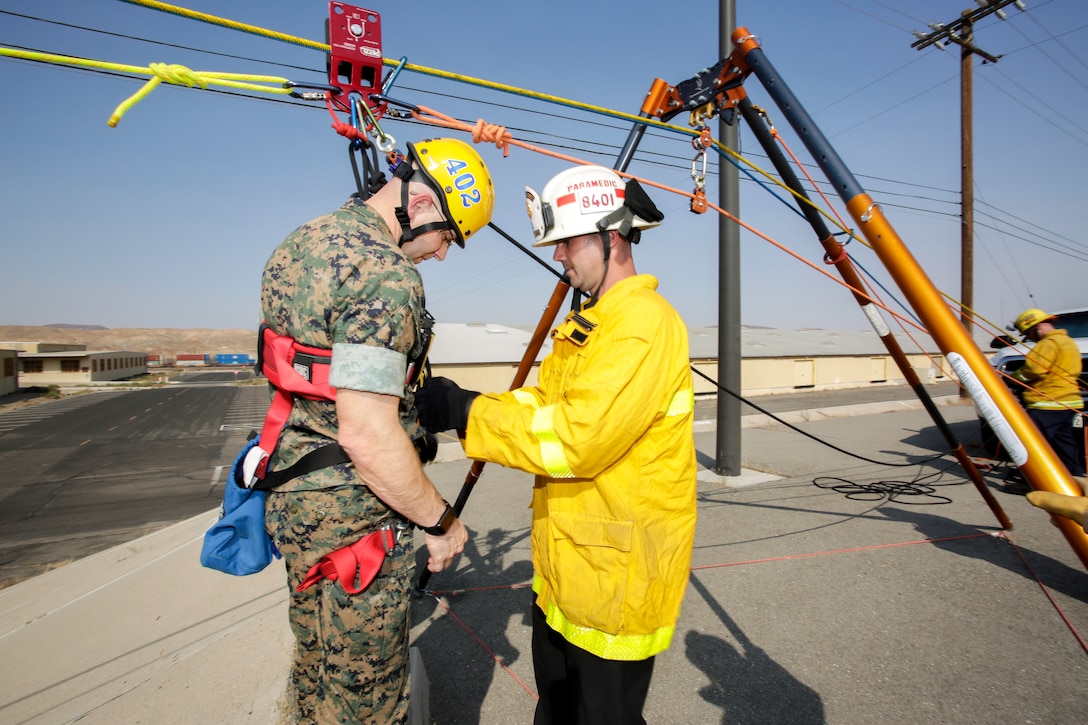 Deputy Fire Chief, Ryan Tworek with Fire and Emergency Services attaches a harness to Col. Craig C. Clemans, commanding officer, so he can be hoisted over a street in a simulated Swift Water Rescue Training course held aboard Marine Corps Logistics Base Barstow, California, Sept. 23.