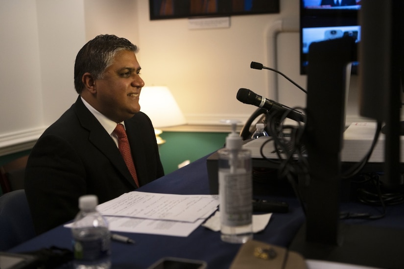 A man speaks into several microphones as he looks at a laptop.