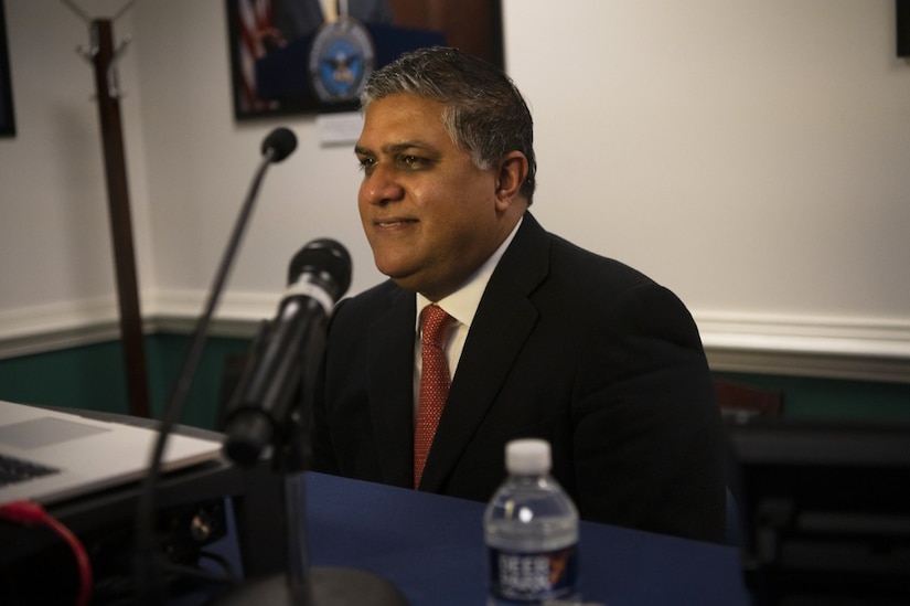 A man in a suit sits at a table and looks ahead.