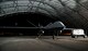 An MQ-9 Reaper sits under an aircraft sunshade with a bright light shining on it from the right side of the photo.