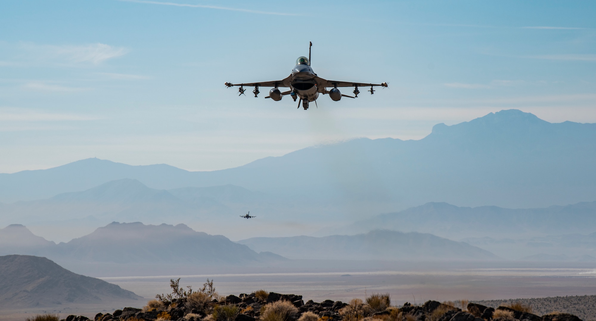 Two F-16s fly over mountain.