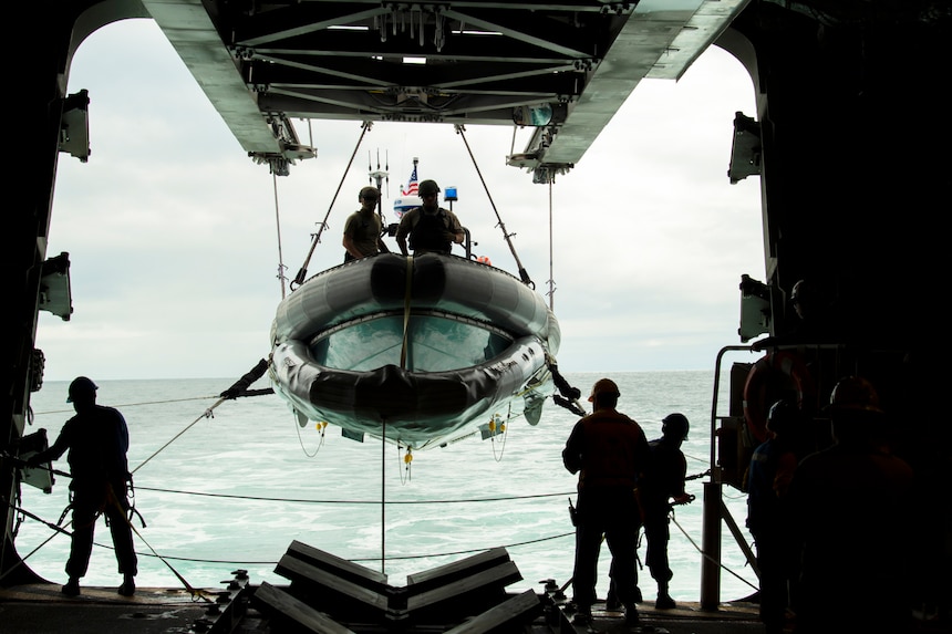 A small inflatable boat is lowered into the ocean.