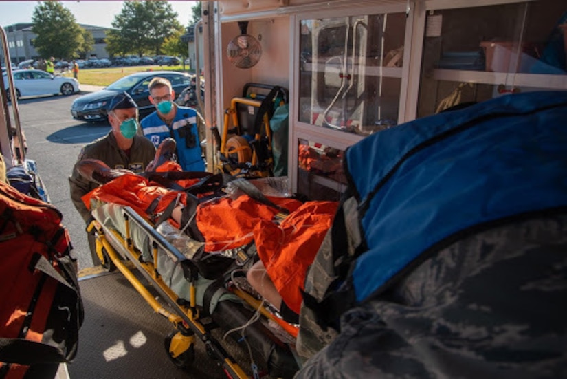 Airmen wearing masks lift a patient into an ambulance.