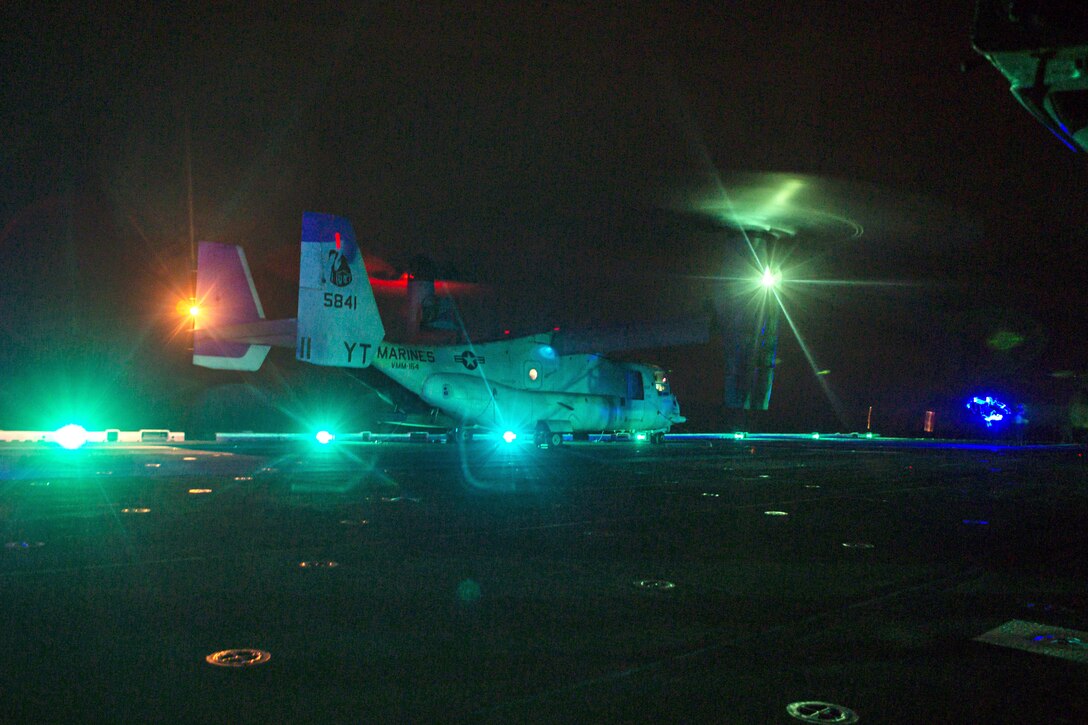 A military aircraft gets ready to take off from a large ship at night.