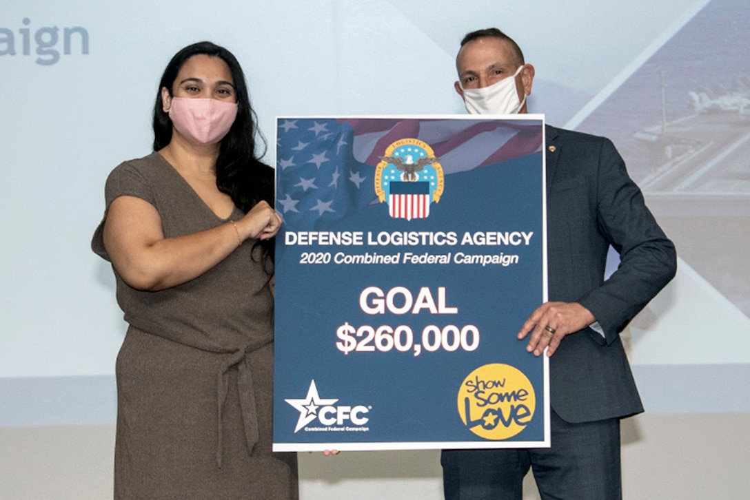 Man and woman wearing face masks over their mouth and nose hold a blue sign that reads Defense Logistics Agency 2020 Combined Federal Campaign Goal $260,000.