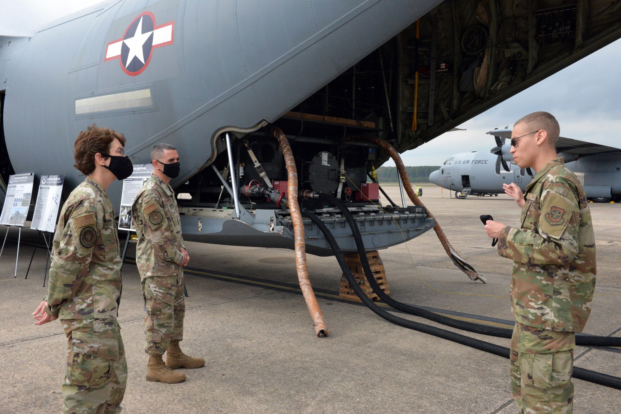 Large machine in back of plane with hoses hanging out and man explaining its uses to commander