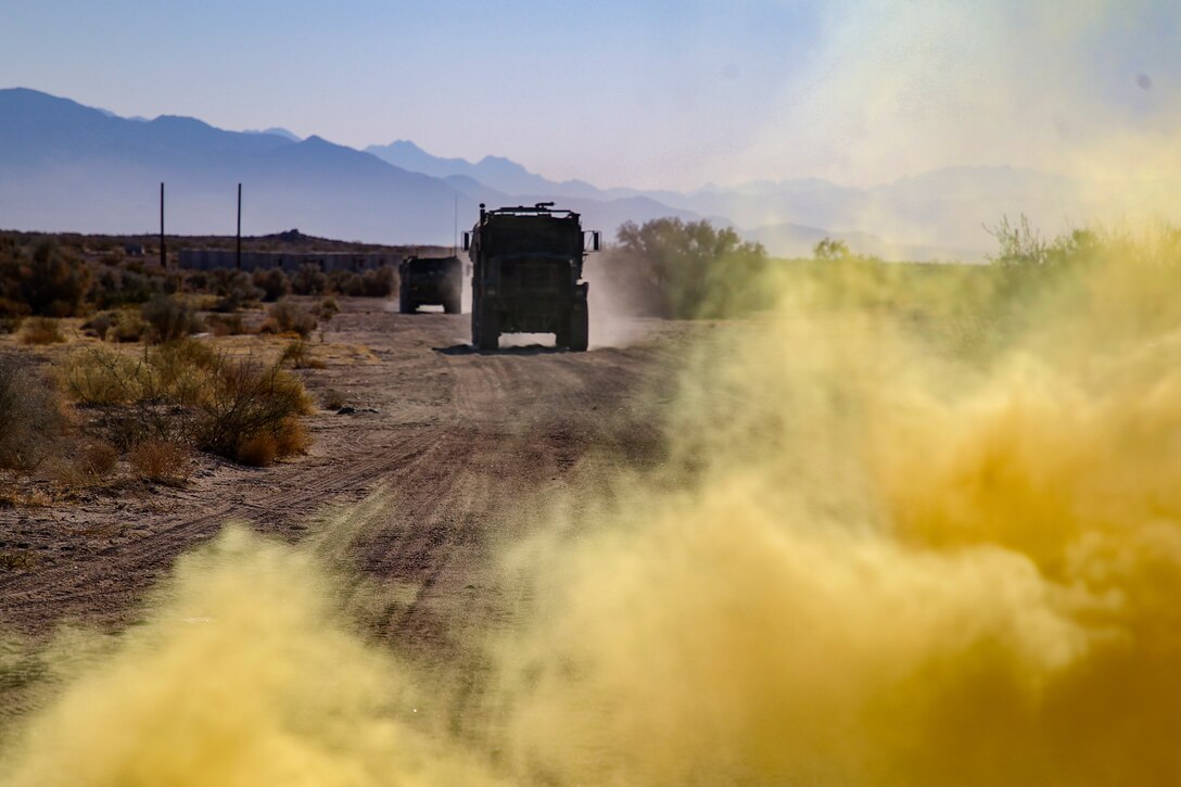 Two trucks drive on a dirt road near clouds of yellow smoke.