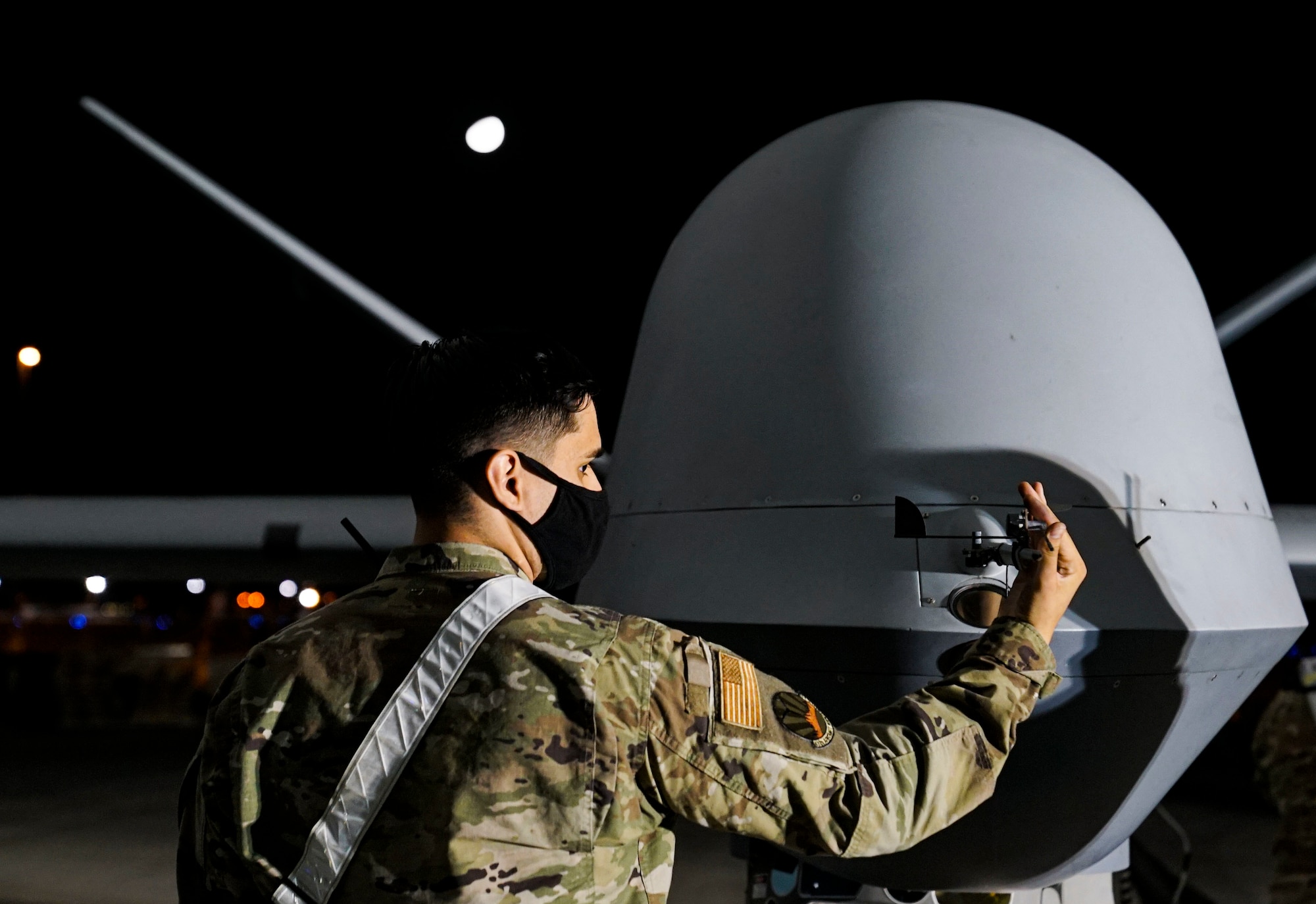 An MQ-9 Reaper maintainer checks the front nose of an MQ-9 during a preflight inspection at night.