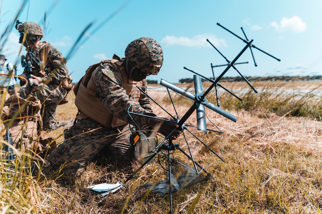A Marine sets up a communications system in a large field.
