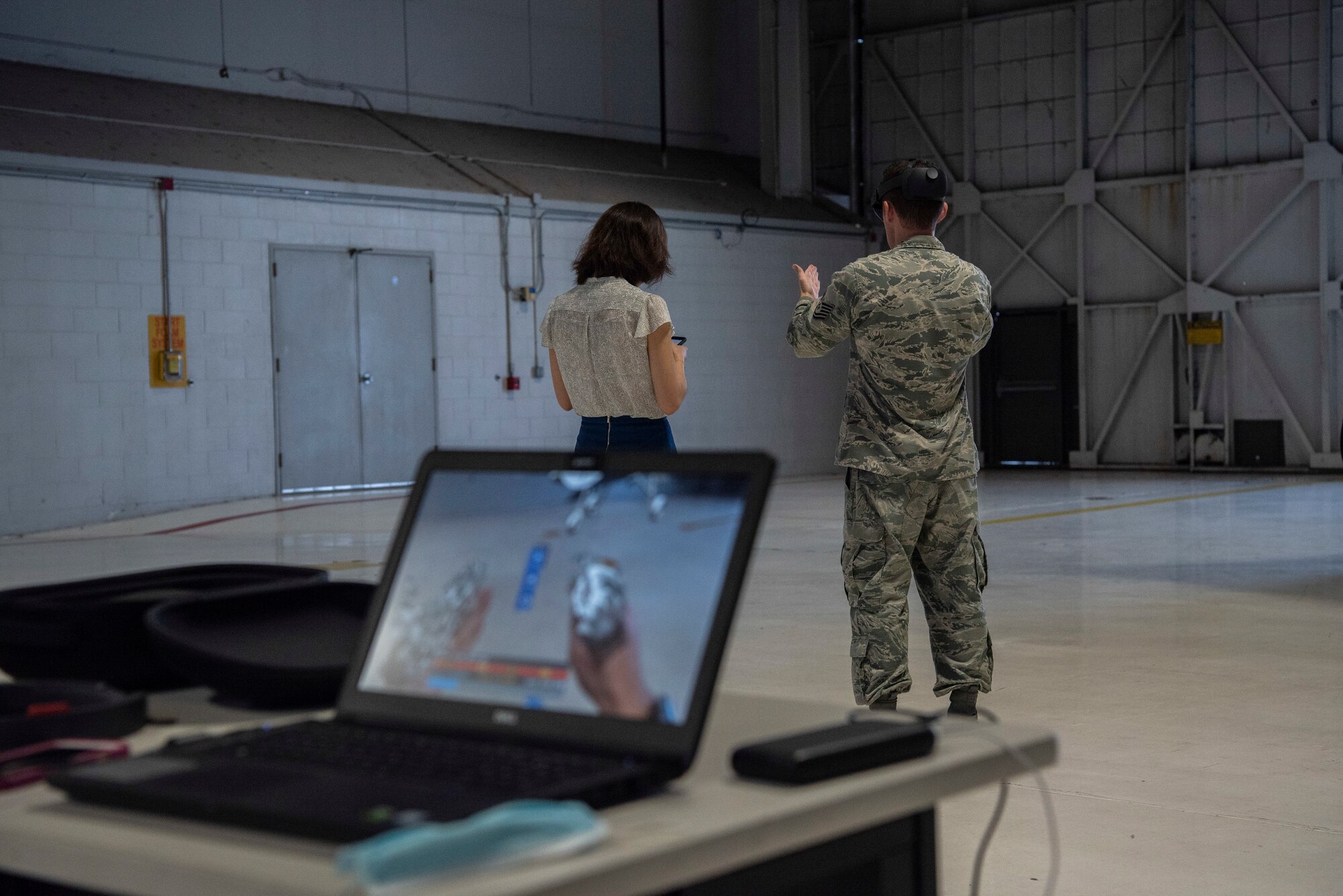 A contractor takes notes on her cell phone as an Airman uses an augmented reality headset.