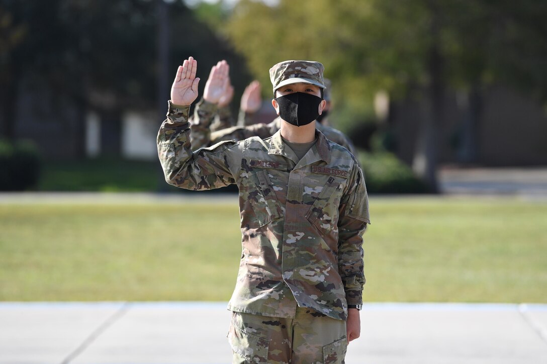 A line of airmen hold their right hands up as they recite an oath of enlistment.
