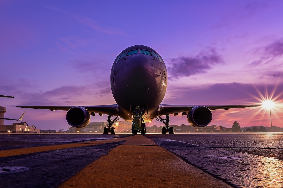 A large military aircraft sits on a runway with a purple sky at sunrise.