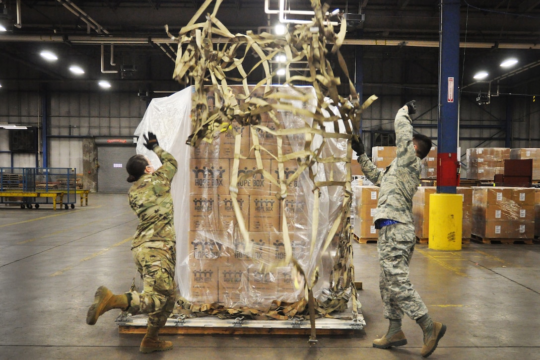 Two airmen prepare a large stack of boxes on a pallet.