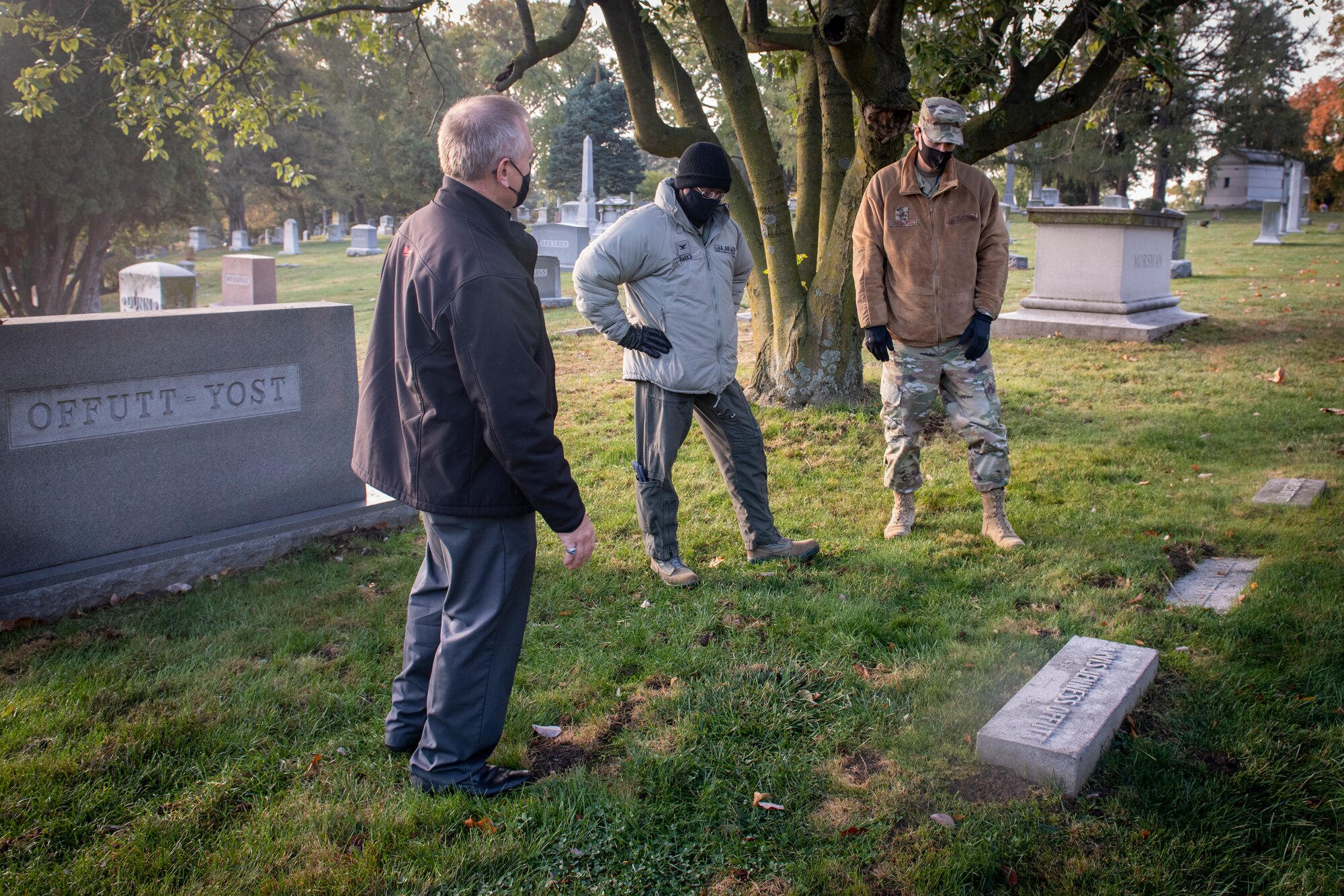 Two service members and a civilian stand at a grave site.