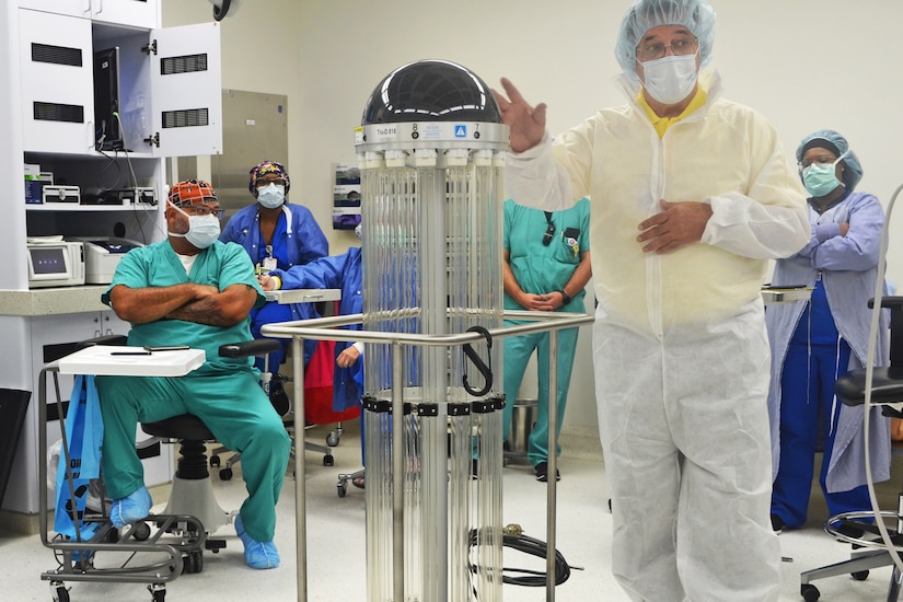 A man dressed in personal protective gear demonstrates a robot to people dressed in surgical scrubs.